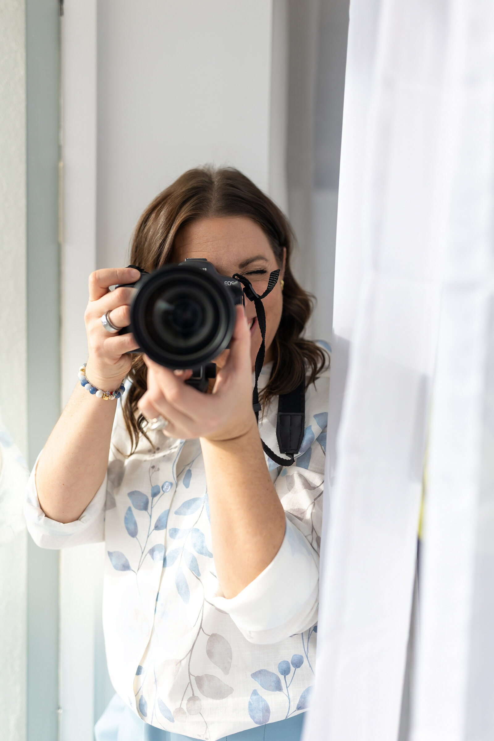Heather Bienz photographing with her camera beside a sunlit window.